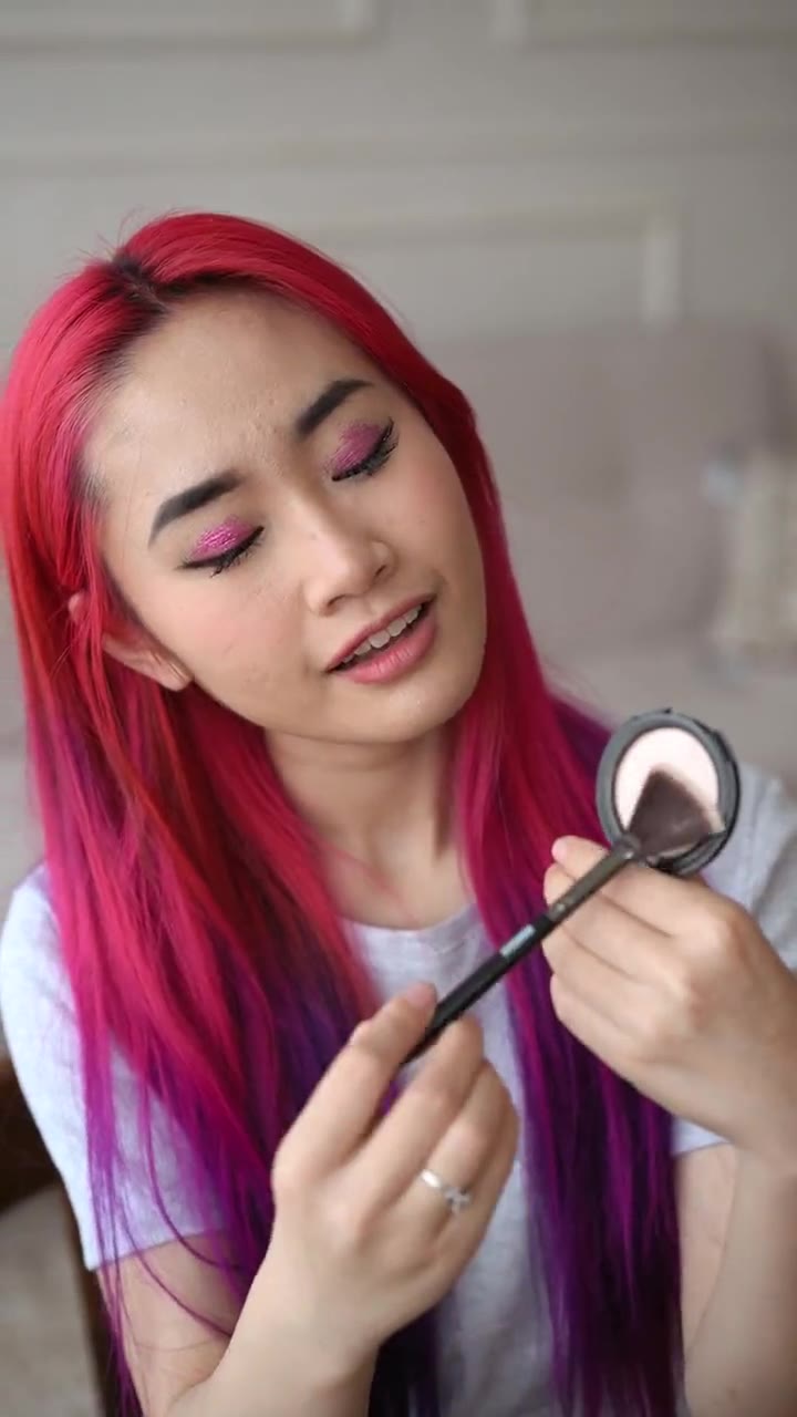 Modelo de cabelo rosa aplicando blush com pincel