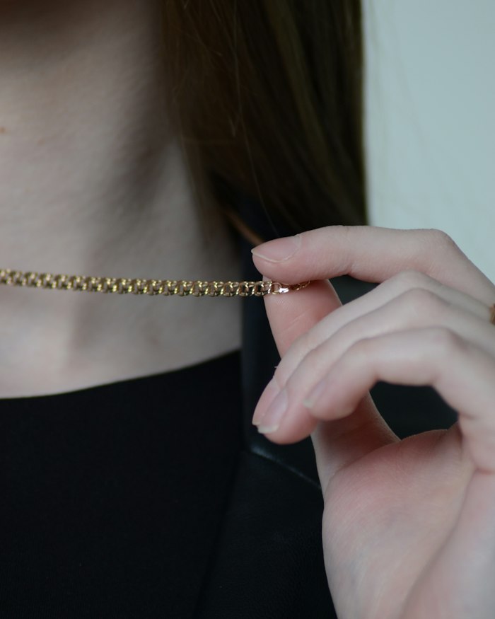 Mãos ajustando um colar dourado fino